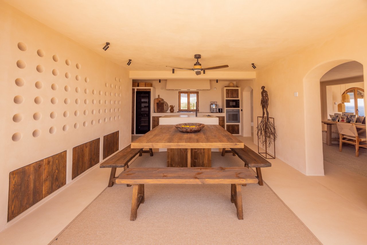 Mesa de madera y pared de huecos circulares con la cocina al fondo