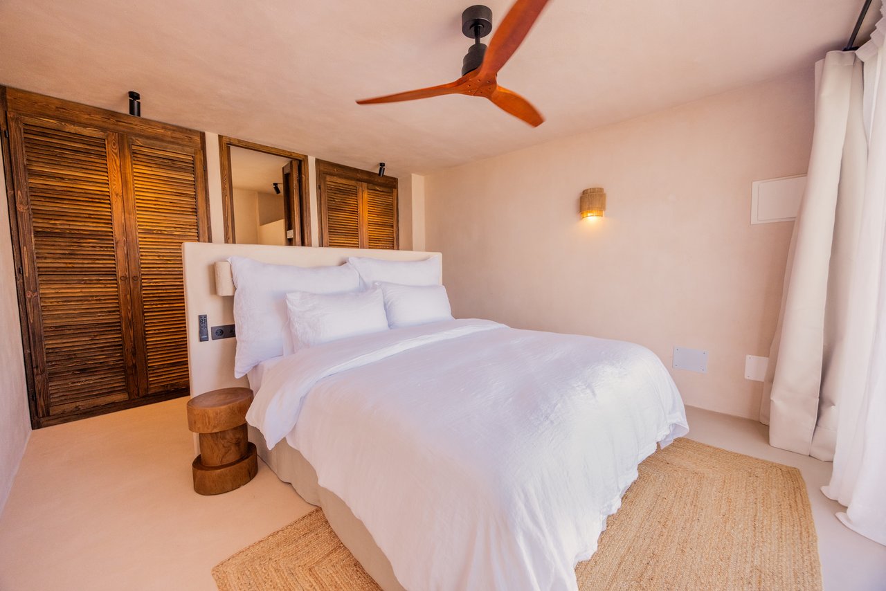 Habitación 02: cama blanca, armarios de lamas y ventilador de madera